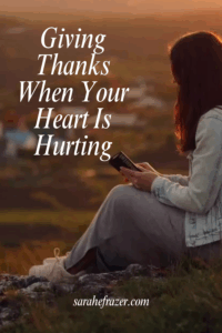 woman sits on ground with open bible text overlay reads: giving thanks when your heart is hurting
