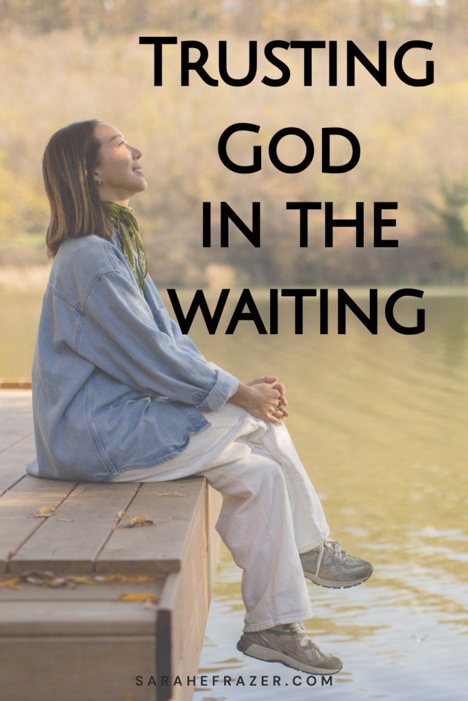 Woman sits on a dock looking at the sky with a peaceful expression on her face text overlay reads: trusting God in the waiting