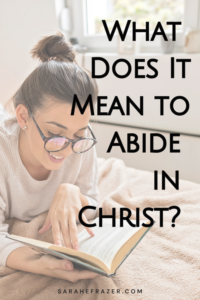 Woman reads her Bible lying on a bed. Text reads: What does it mean to abide in Christ Jesus